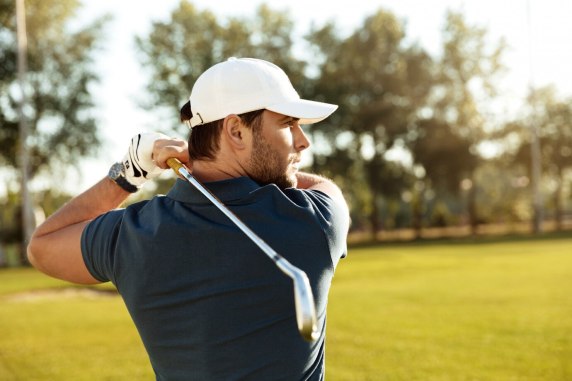 A golfer finishes his golf swing on the sun‑dappled grassy fairway.
