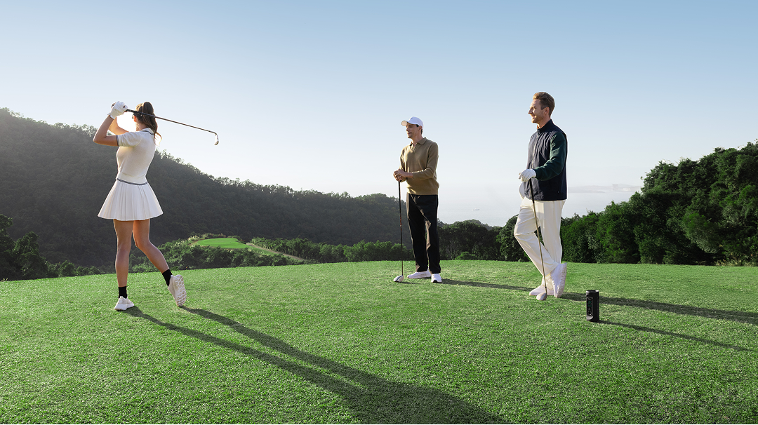 Female golfer swinging club with two golfers watching on course