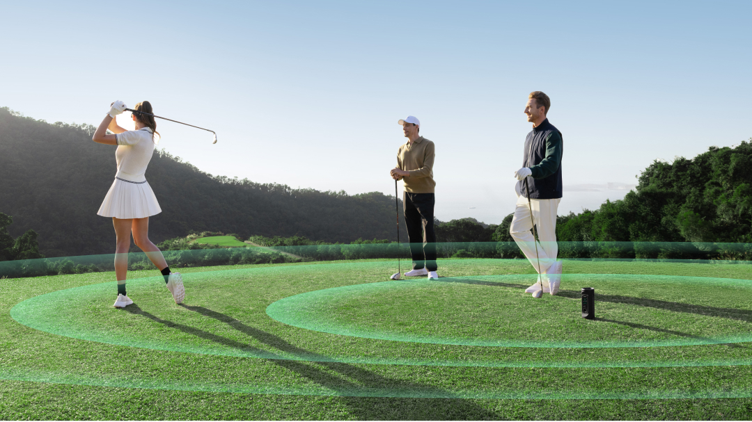 A female golfer swinging a club while two male golfers watch, the MILESEEY GeneSonic Pro Detachable GPS Speaker placed on the ground with illustrated sound waves