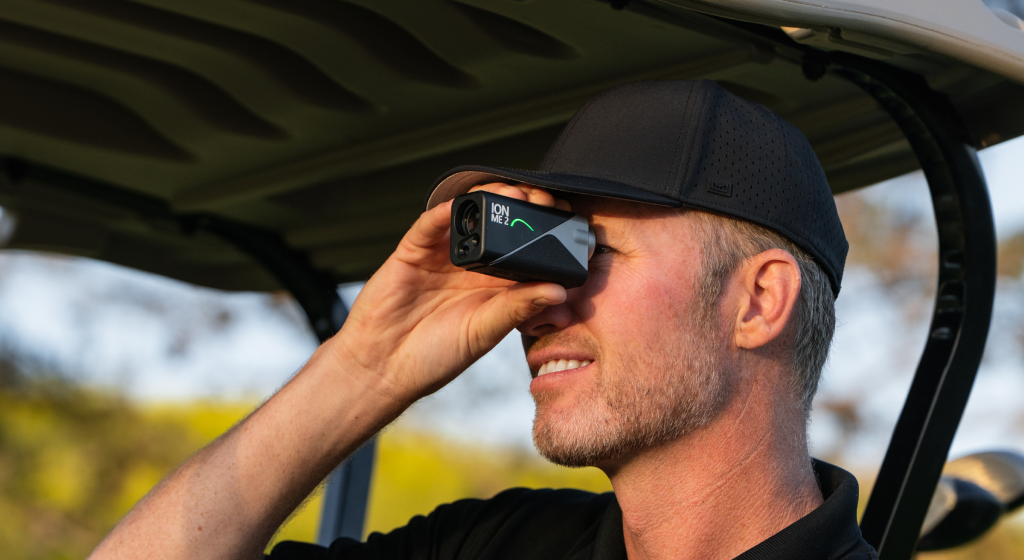 Golfer in a black cap using the Mileseey IONME2 rangefinder from inside a golf cart