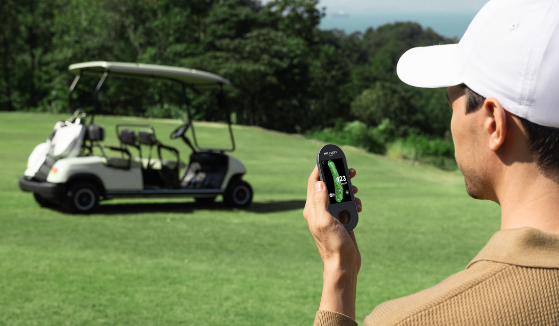 Golfer holding the MILESEEY GeneSonic Go Golf GPS Handheld on the course with a golf cart in the background