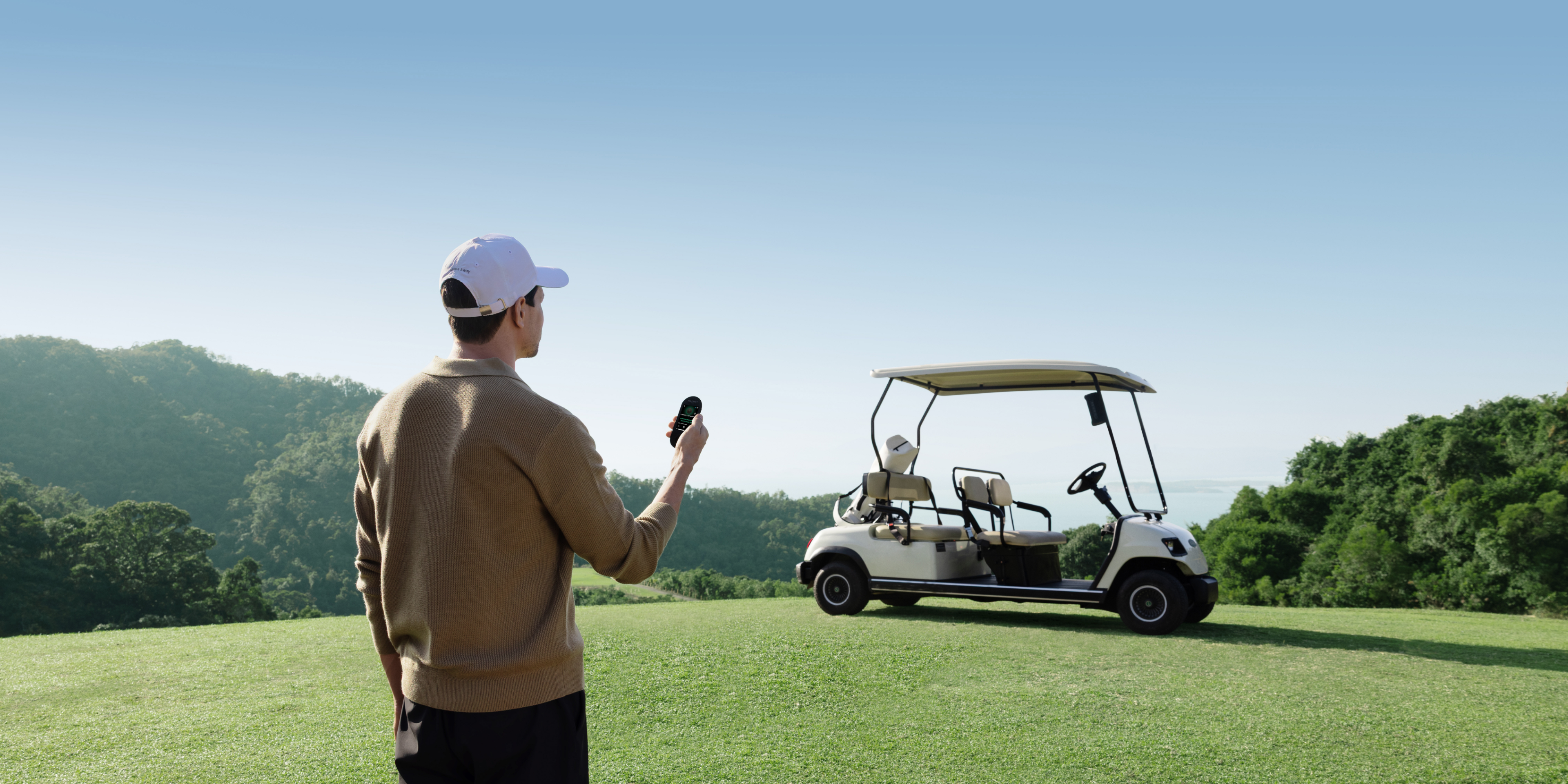 Golfer using a handheld GPS device near a golf cart on the course