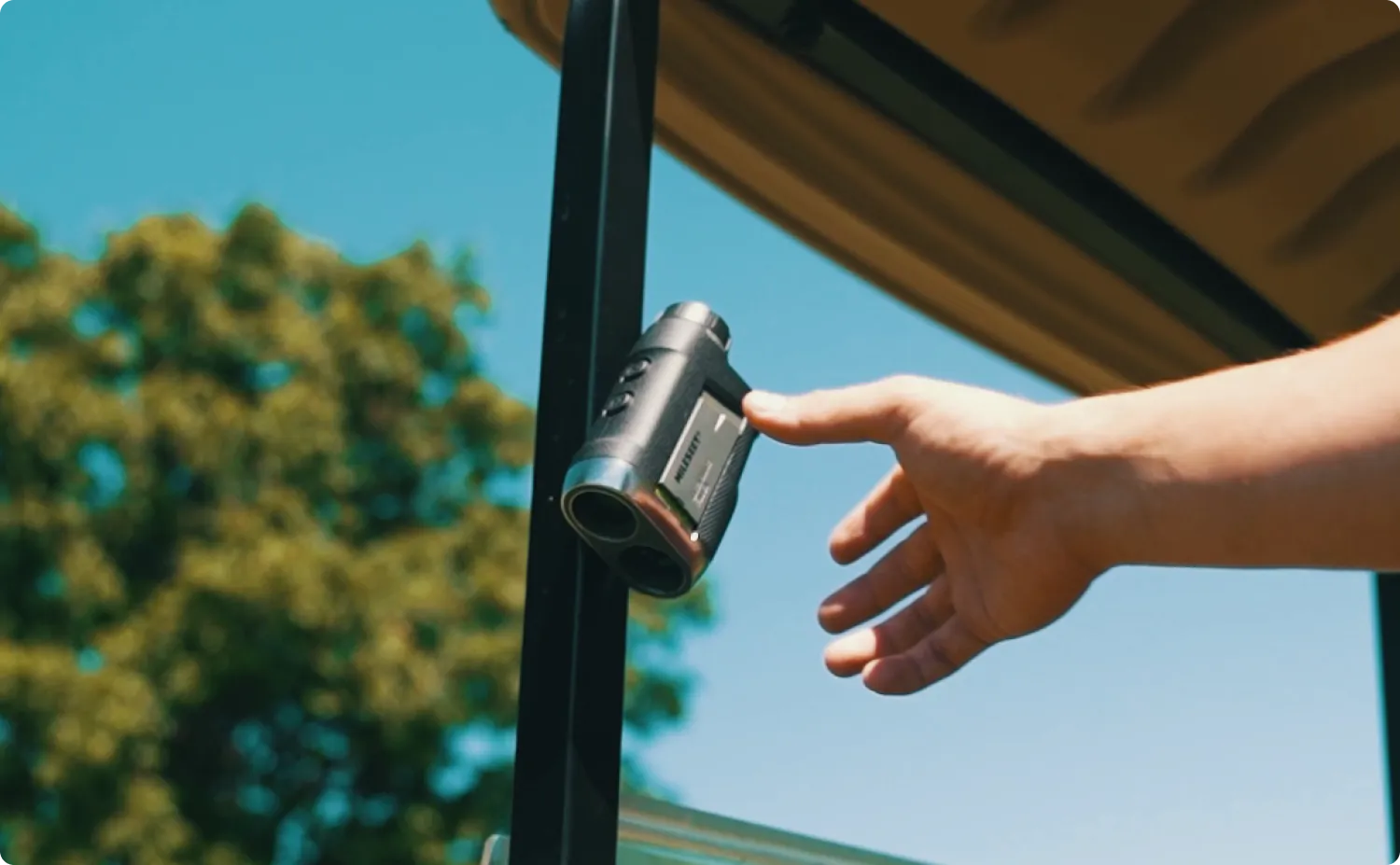 Hand reaching toward the Mileseey PF260 Tour rangefinder mounted on a golf cart roof frame