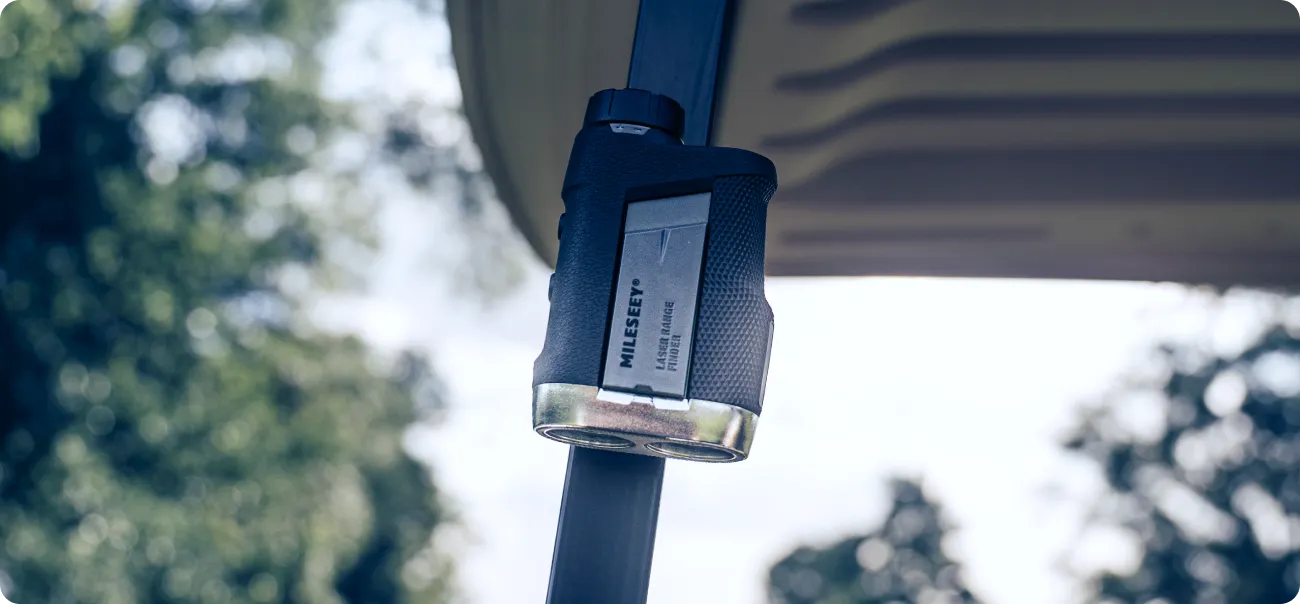 The MILESEEY PF260 Tour golf rangefinder clings magnetically to a golf‑cart frame amid blurred woodland.