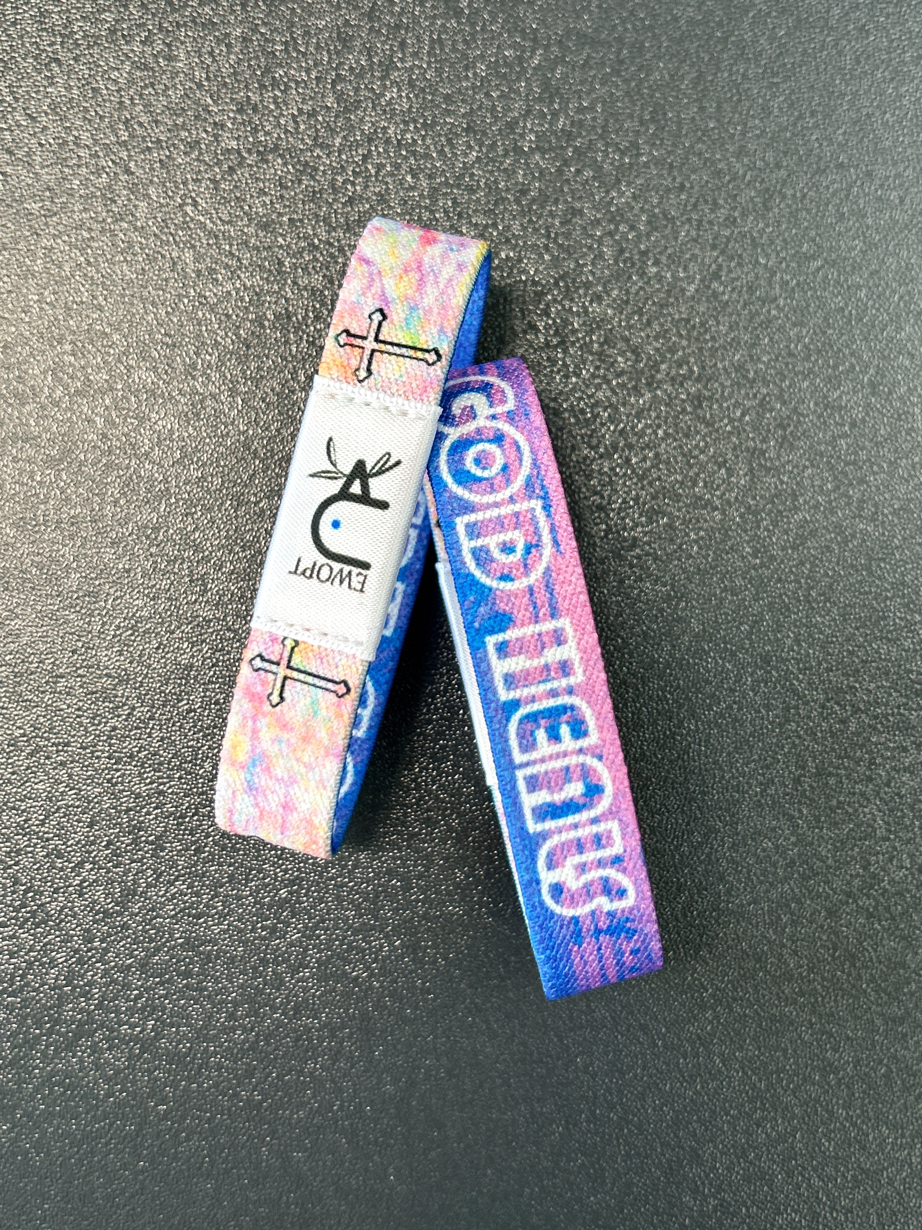 {"default":"A waterproof yappybracelet wristband by EWOPT, featuring a soft gradient of blues, pinks, and purples. A black cross and the word “GOD” in white stand in contrast, creating a fresh and faith-inspired visual effect. Made from high-quality waterproof materials and equipped with NFC functionality, it offers daily inspiration by connecting to Daily Bible content."}