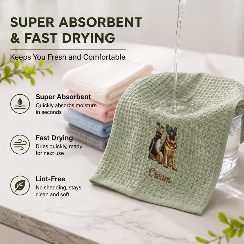 May include: A stack of waffle-textured towels in white, pink, blue, and gray, with a sage green towel featuring an embroidered German Shepherd and the text Cream. Water pours onto the green towel, highlighting the super absorbent and fast-drying features.