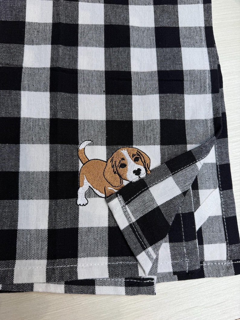 May include: A black and white checkered fabric with an embroidered beagle dog. The dog is brown and white with black accents. The fabric is folded over, revealing the underside of the checkered pattern.