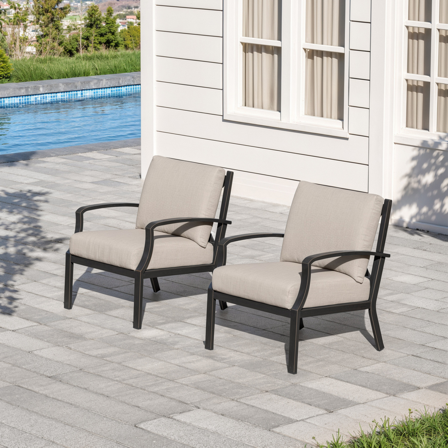 Two cushioned armchairs with dark frames set on a patio near a pool and house wall-Seehill
