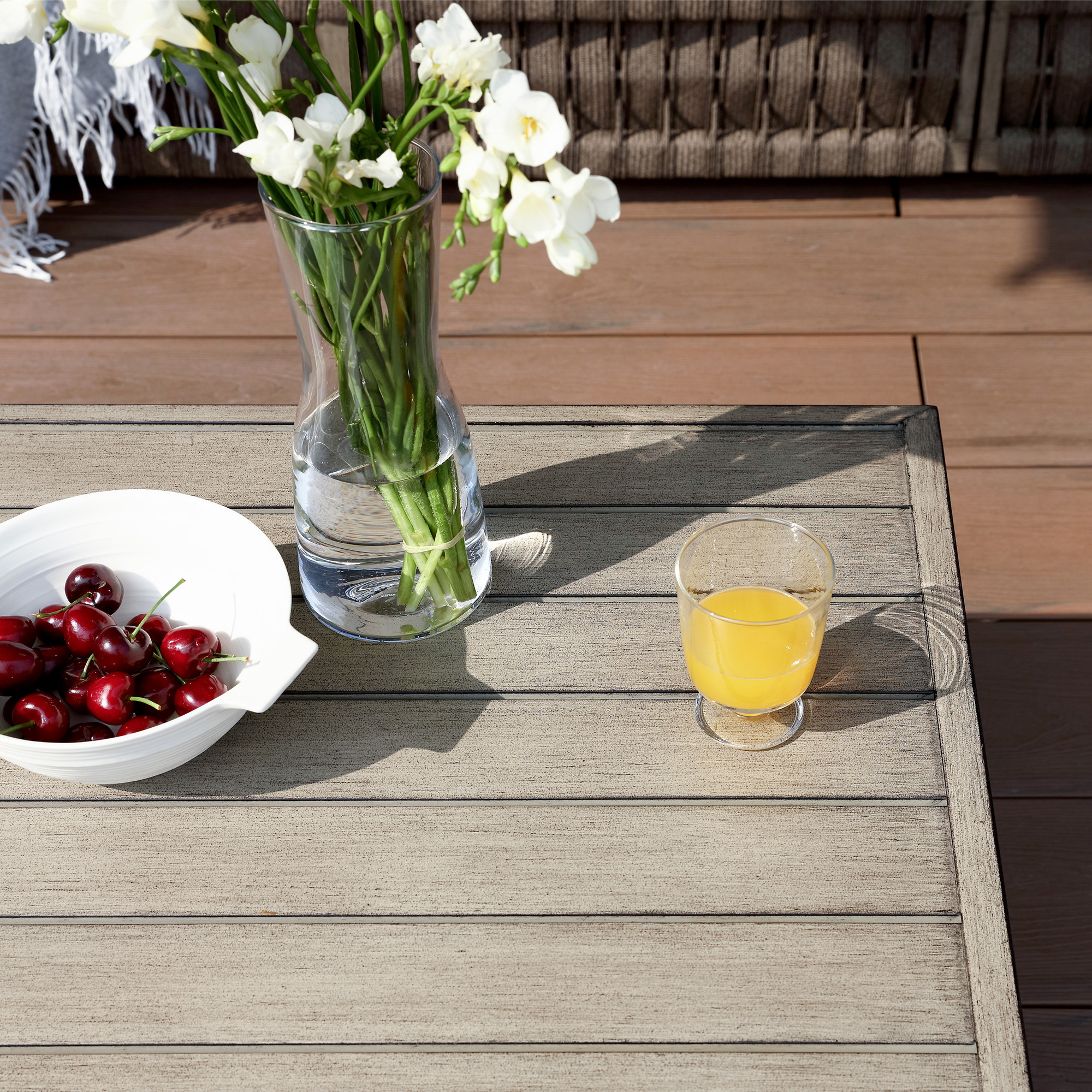 Explore the outdoor wooden table with a vase, bowl of cherries, and glass of juice in this exclusive outdoor setting. - Seehill