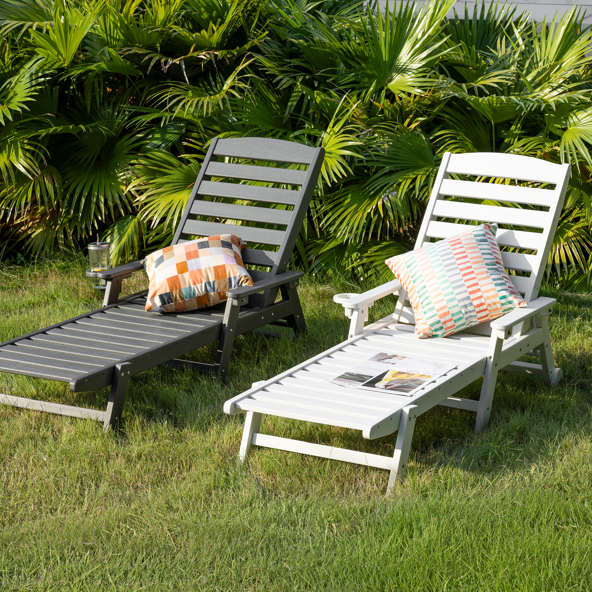 Two adjustable outdoor lounge chairs with colorful pillows on green grass near tropical plan-Seehill