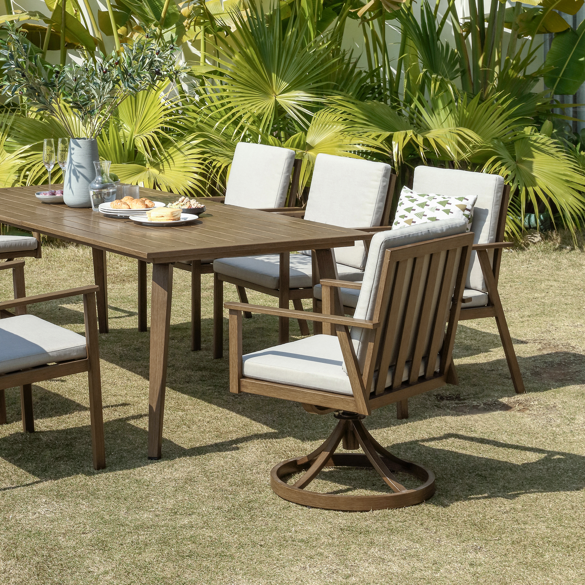 Crafted with a teak outdoor dining set featuring swivel chairs and light gray cushions, this piece enhances any outdoor space. - Seehill