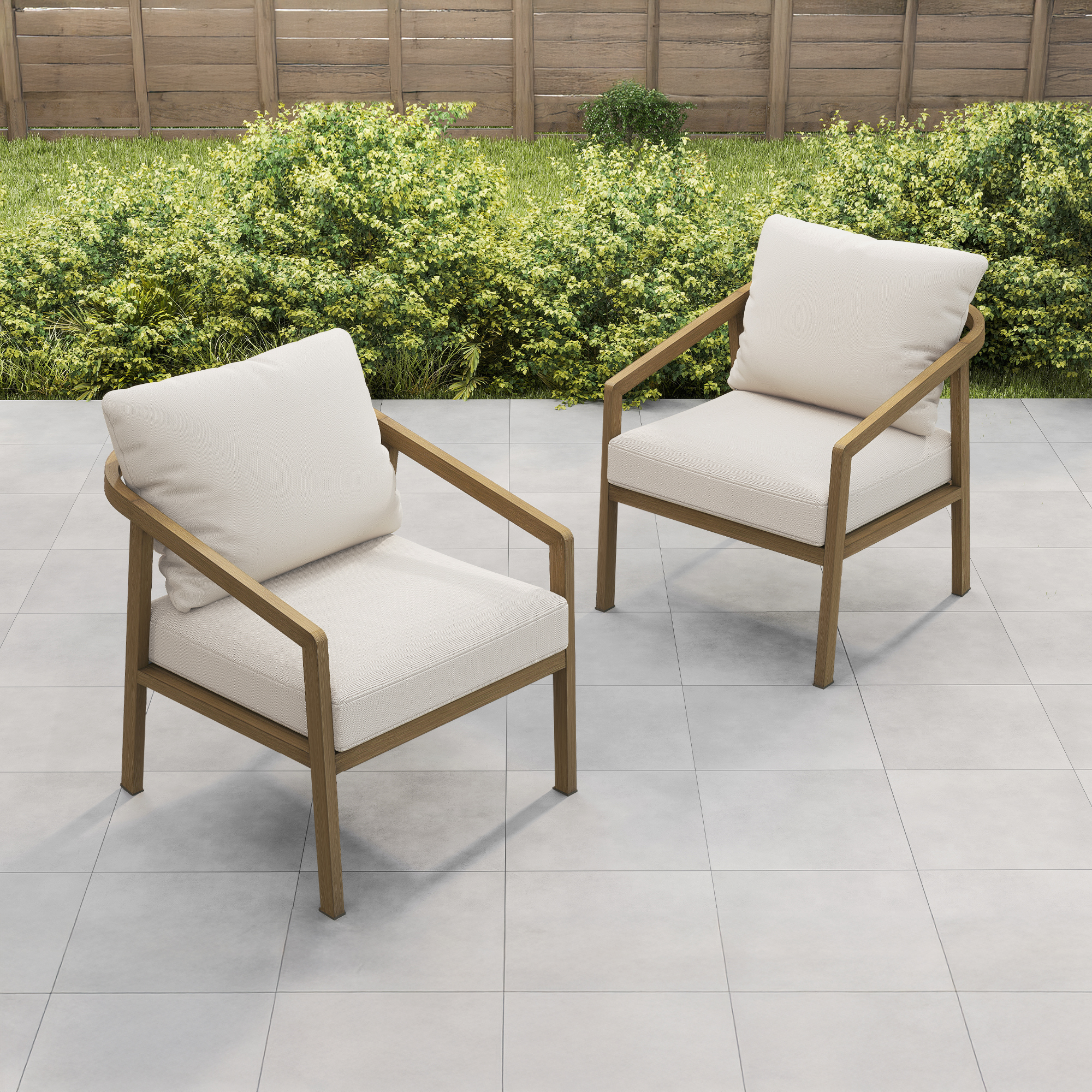 Two cushioned outdoor armchairs with wooden frames on a tiled patio near green bushes-Seehill