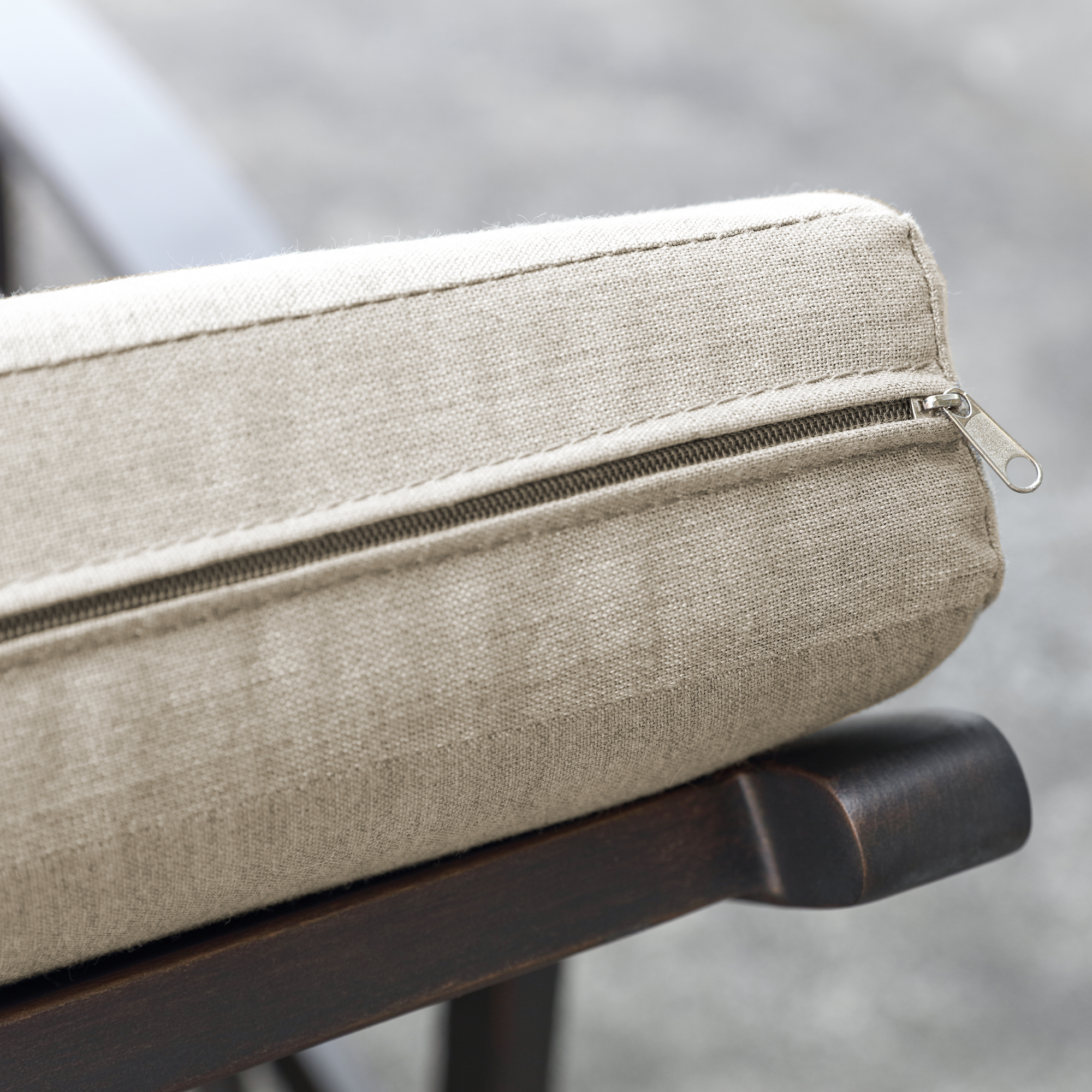 Close-up of beige cushion with zipper detail on dark wooden frame of outdoor lounge-Seehill