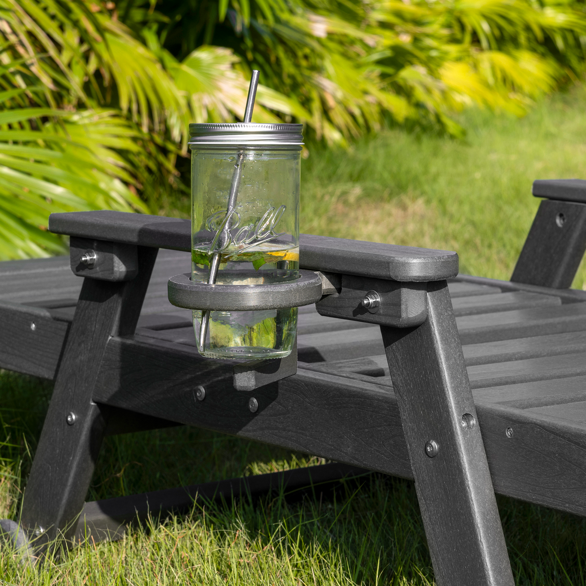 Close-up of a dark gray outdoor lounge chair with a cup holder and glass jar on grass-Seehill