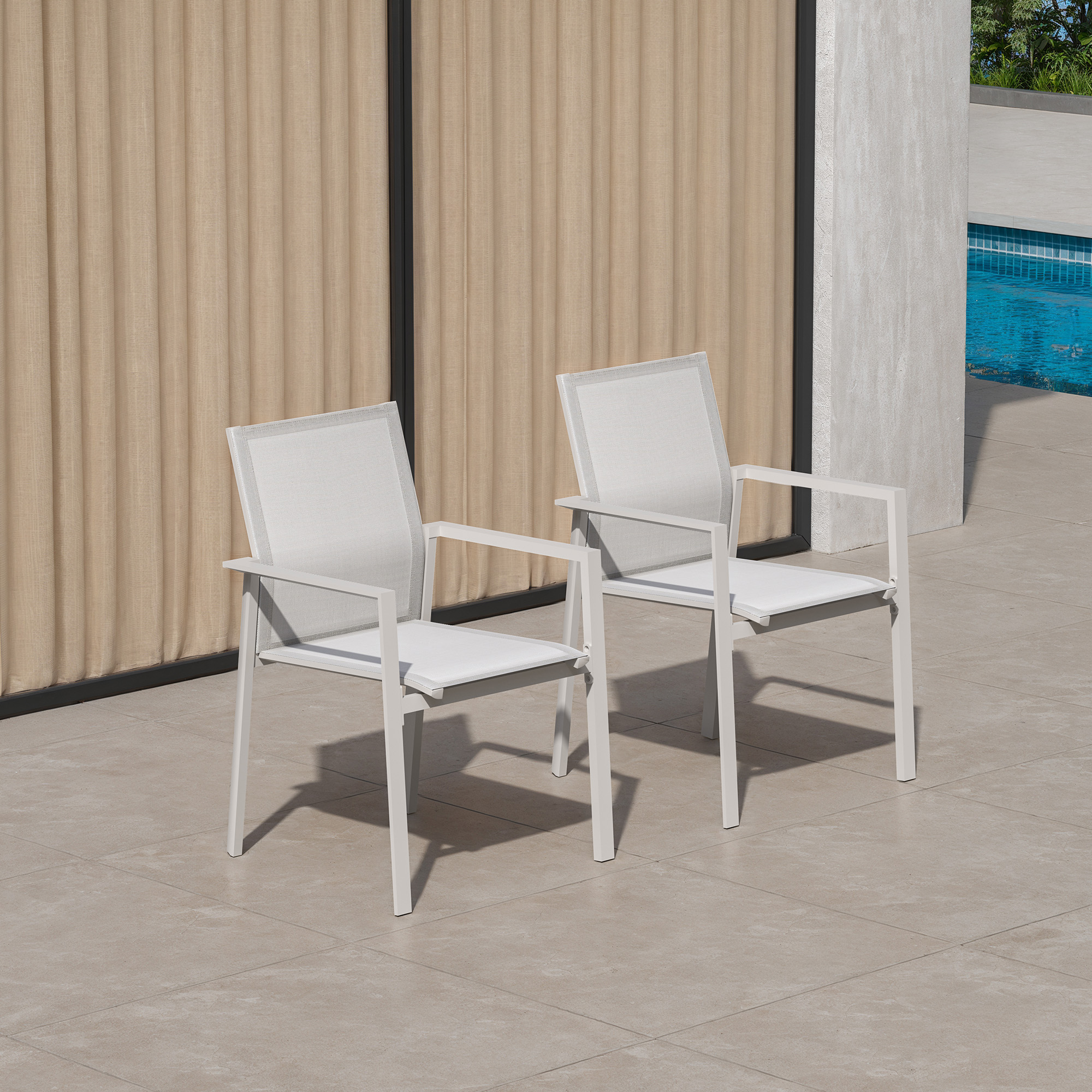 Two white stackable patio dining chairs with full backs set on a tiled poolside patio-Seehill