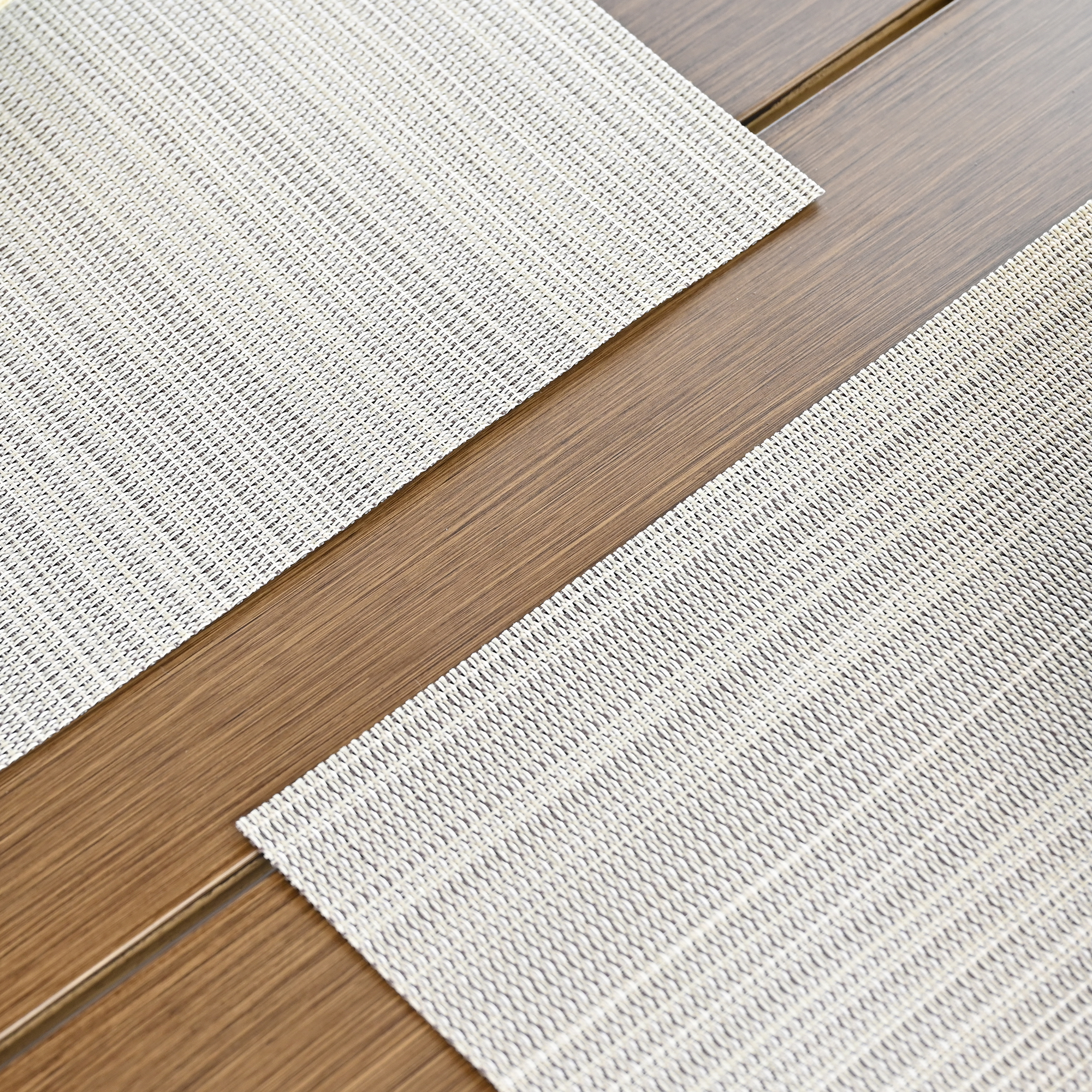 Experience a set of four beige versatile clean look placemats with a subtle texture on a wooden table. - Seehill