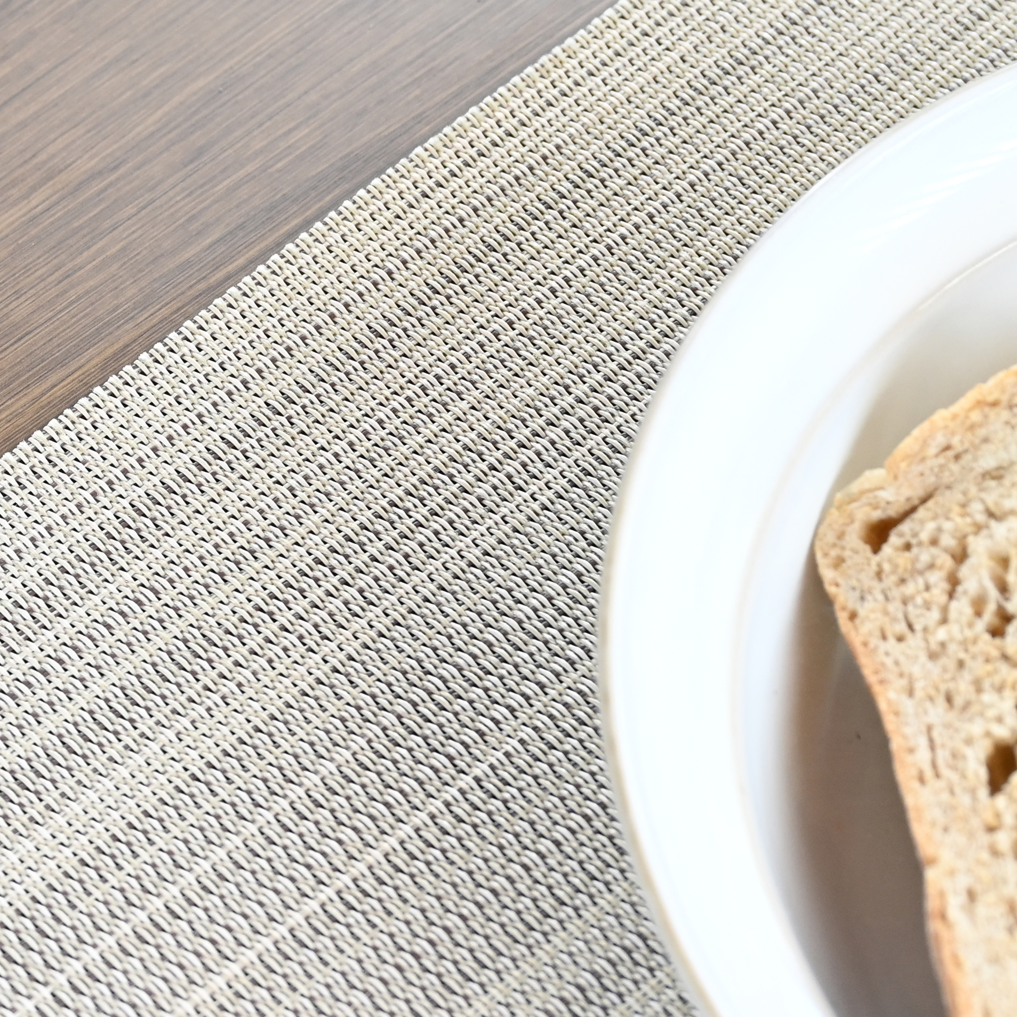 Close-up of a woven textured placemat under a white plate with bread on a wooden table-Seehill