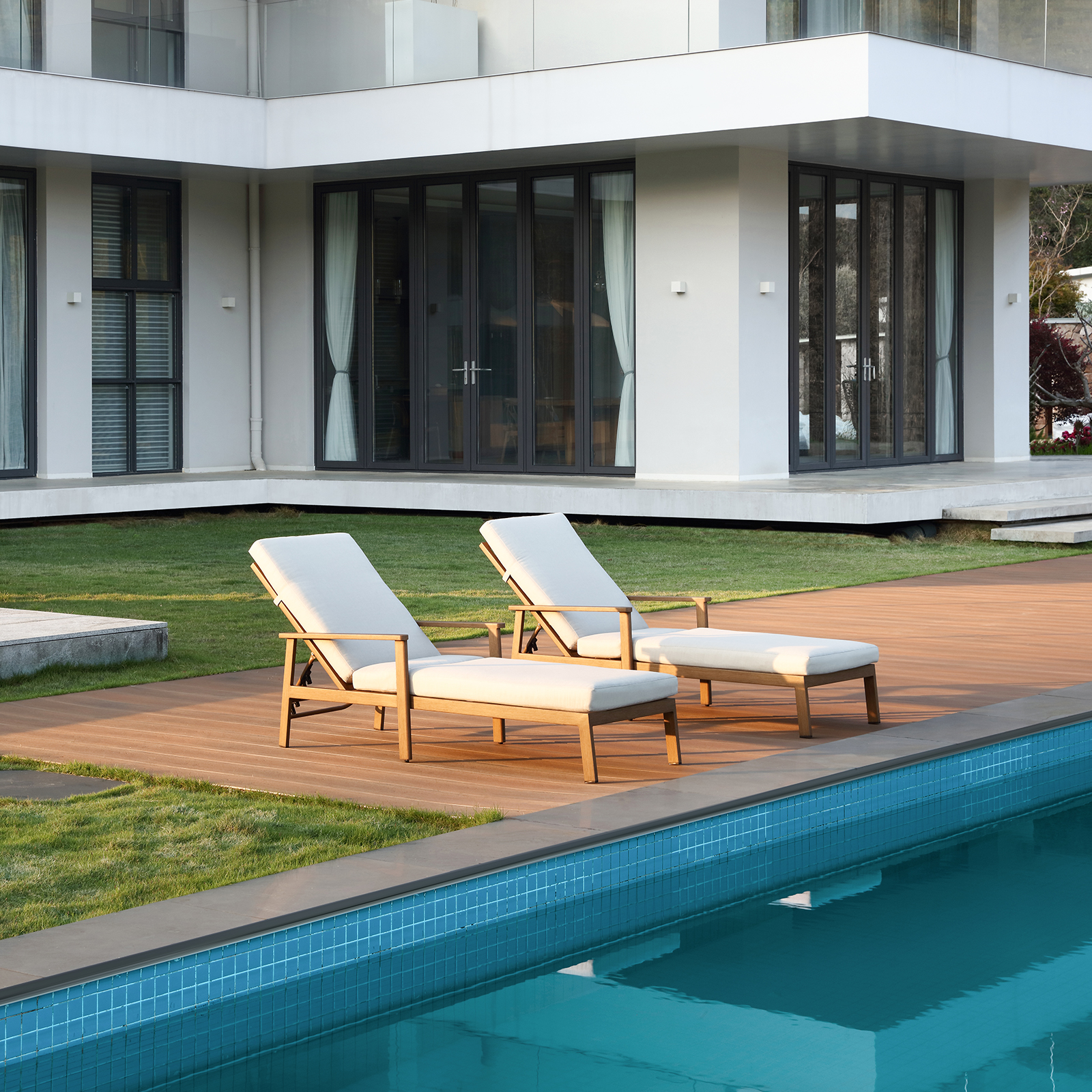 Modern wooden lounge chairs with white cushions by poolside - Seehill