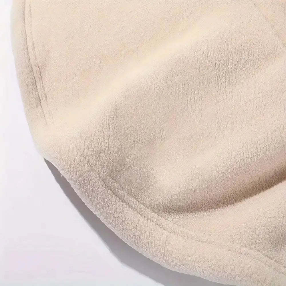 A close-up of a soft, plush fleece fabric in a warm cream or light beige color, showing its textured surface and stitched edge against a plain white background.