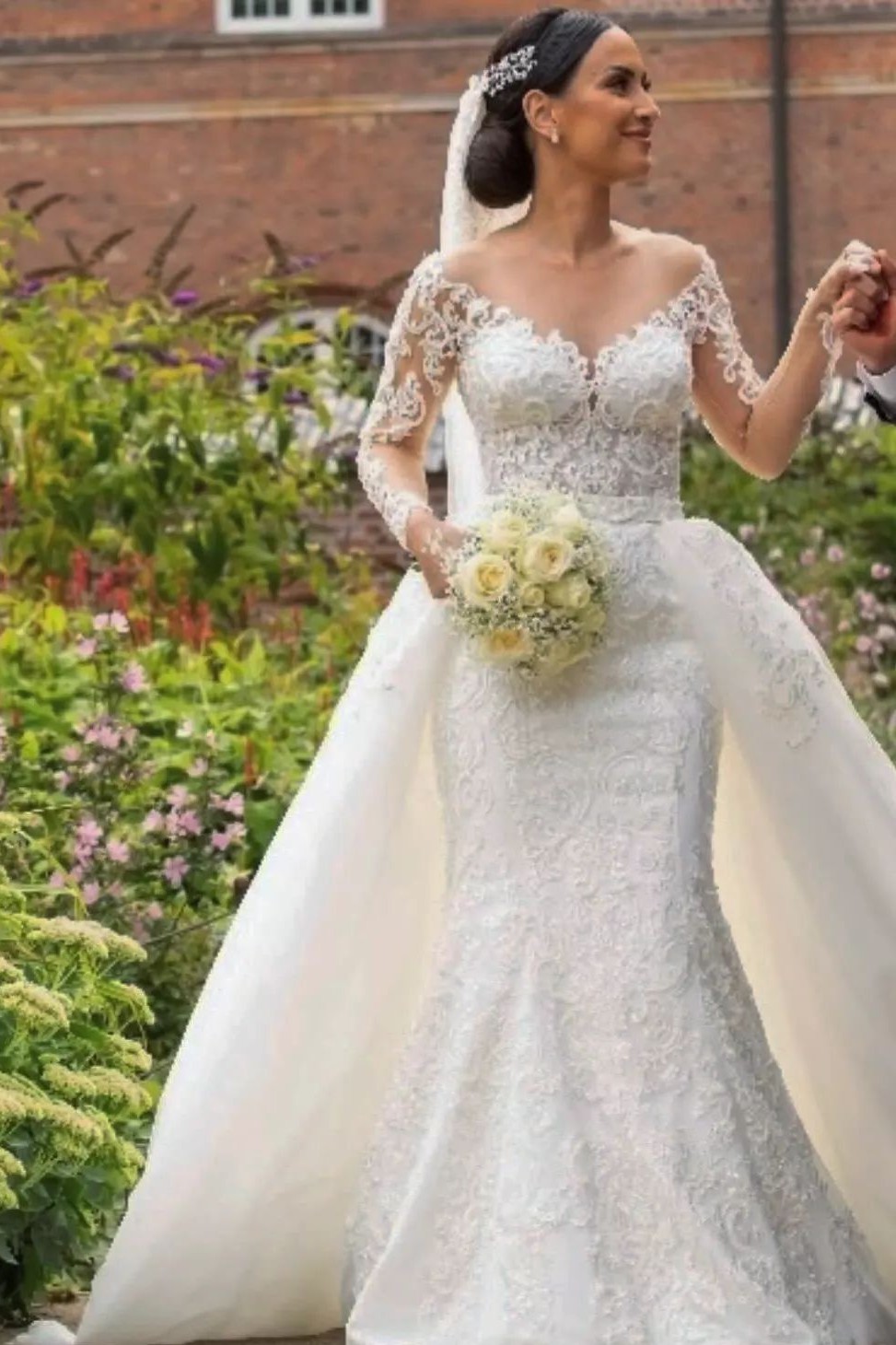 Modest off-the-shoulder lace mermaid wedding dress with long sleeves and a detachable train, showing where the train meets the waist seam