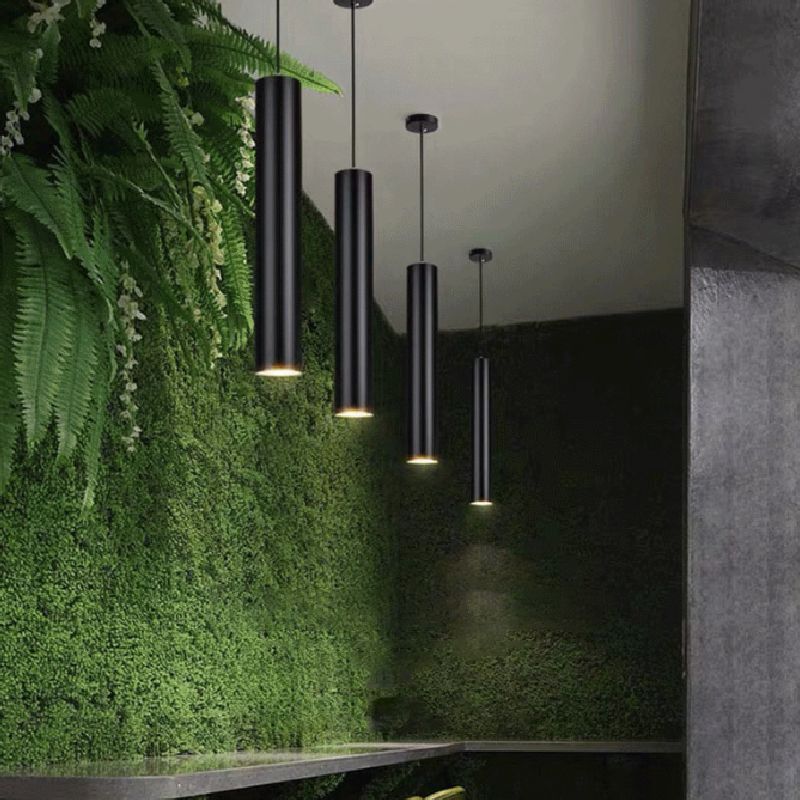 Modern black cylinder pendant lights hanging above a green wall