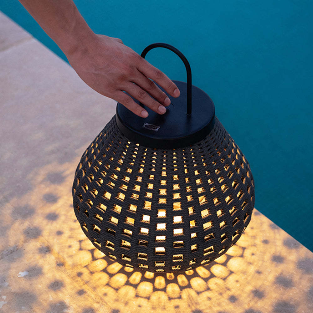 Ritta Outdoor Lantern with warm light, hand reaching.