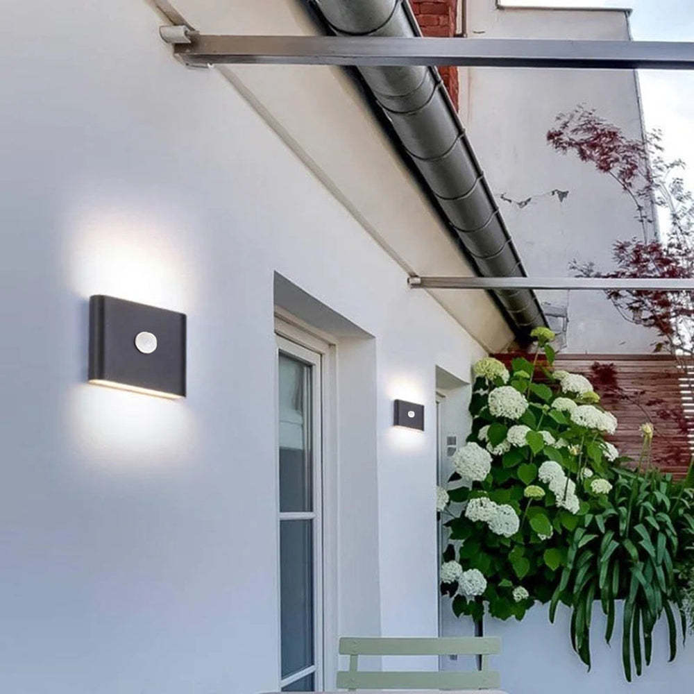 Modern black outdoor wall lamp illuminating a white wall.