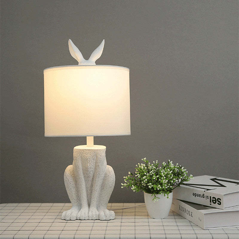 Resin rabbit table lamp with fabric shade and warm light.