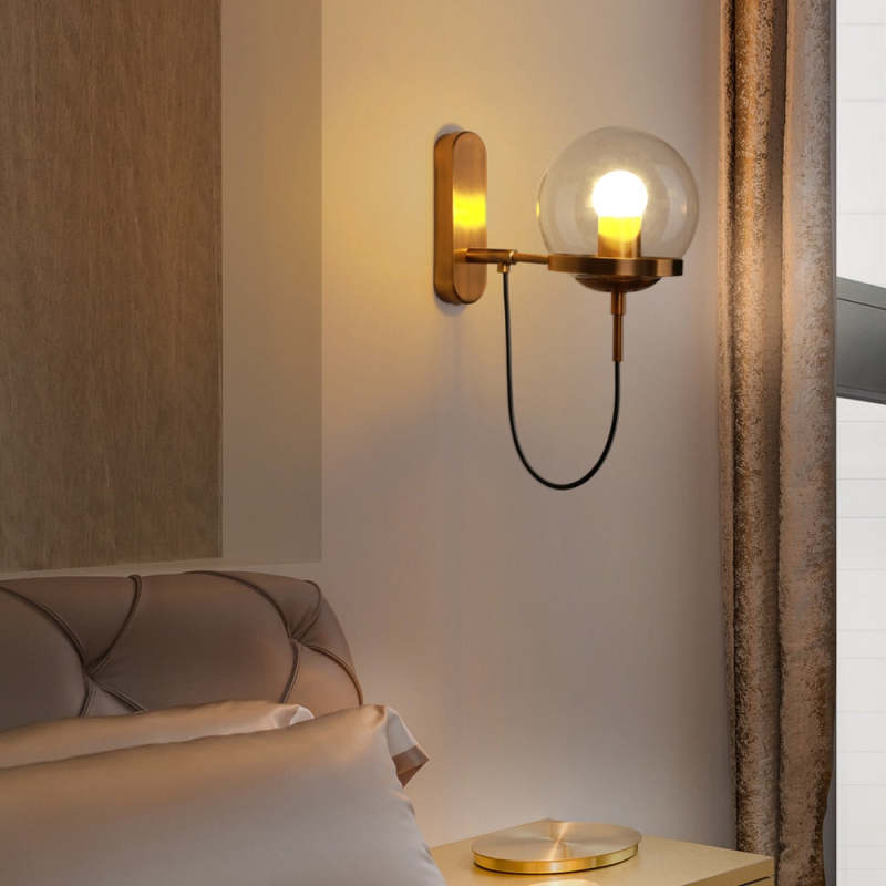 Alessio bronze wall lamp with glass globe in bedroom setting