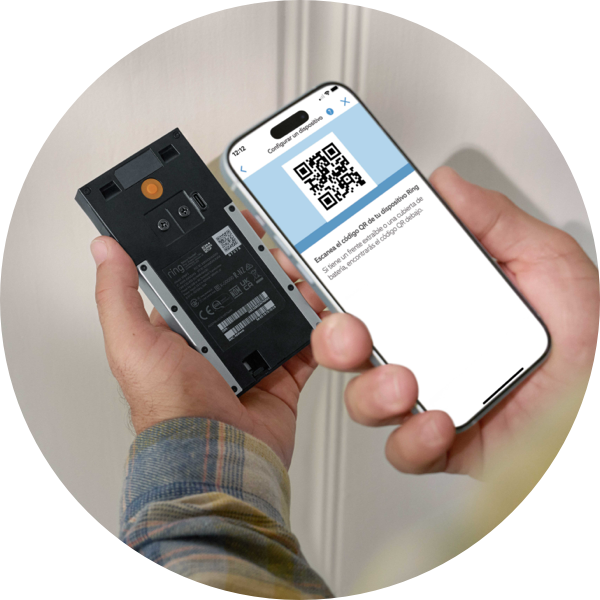 Un par de manos sostienen un teléfono y un Timbre con cámara inalámbrico Ring. La pantalla del teléfono muestra un código QR e indica al usuario que debe escanear el código QR de la parte posterior de su dispositivo.