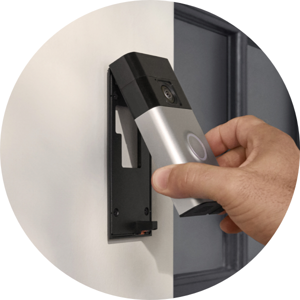 Una mano fija el Timbre con cámara inalámbrico Ring a un soporte instalado al lado de una puerta principal.