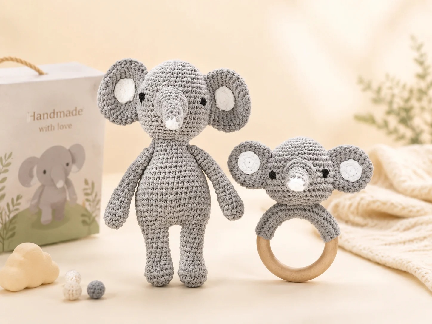 A gray crocheted elephant doll standing beside its matching wooden ring rattle on a white background