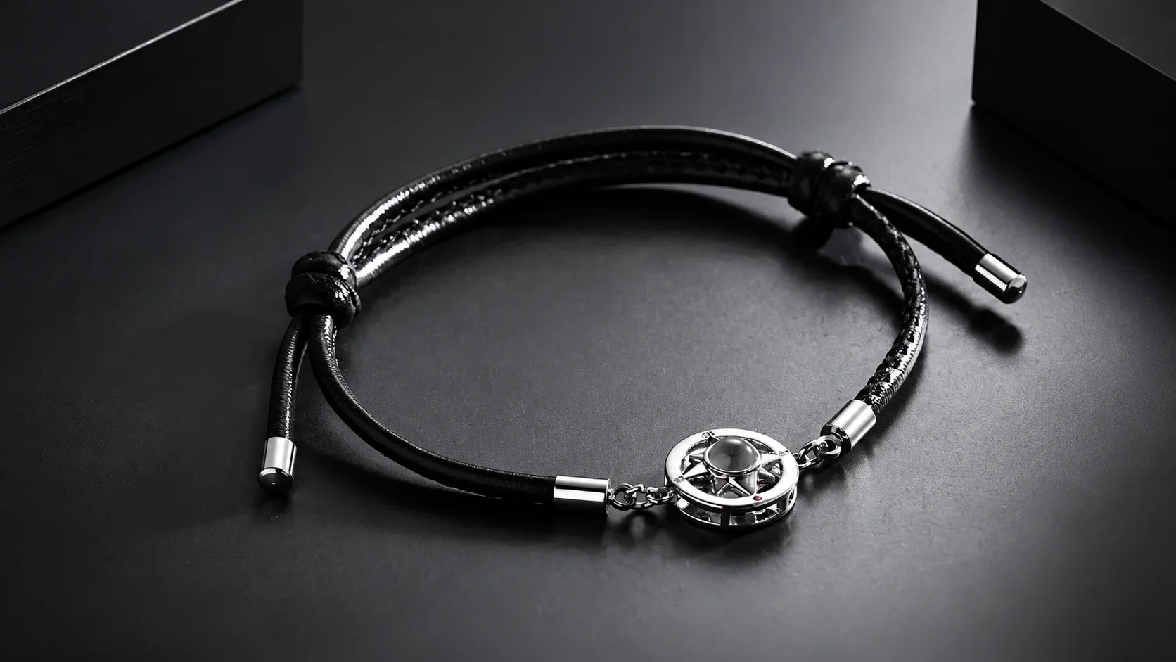 A close-up of the silver compass charm with a round lens center and a small pink accent gem, on a black display surface