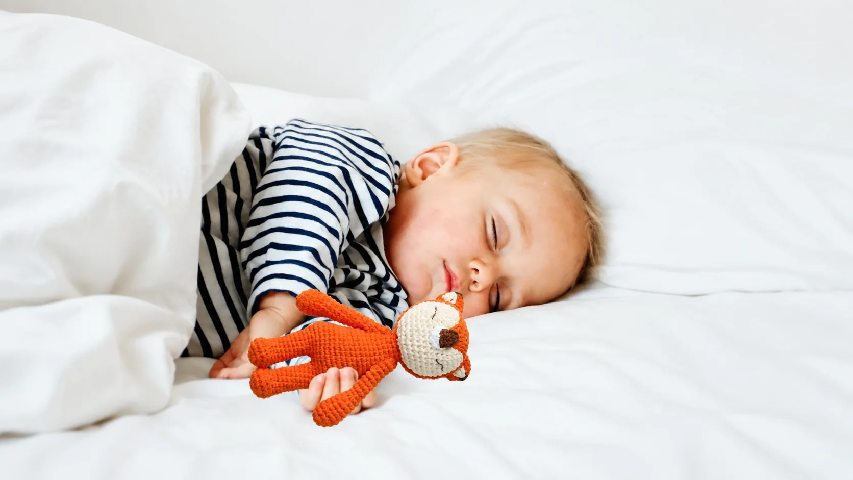 A toddler sleeping peacefully while cuddling an orange crocheted fox doll