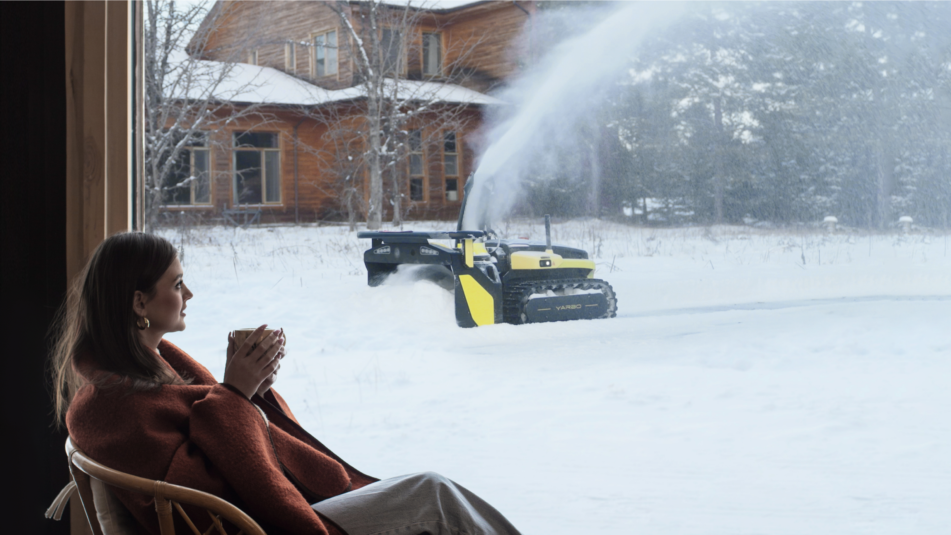 User enjoying coffee indoors while snow blower clears driveway outside.