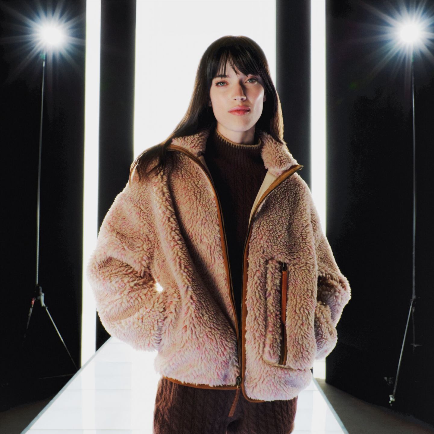 A person wearing the Marlene Confetti Jacket, standing in a black and white catwalk with lights in the background.