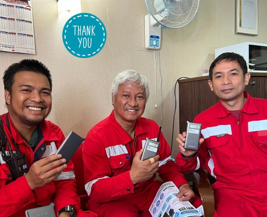Three seafarer customers in red workwear holding portable WiFi devices in a shared onboard space.