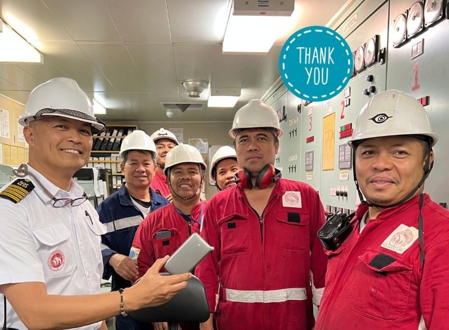 Seafarers in workwear and hard hats pictured with a portable WiFi device aboard a vessel.