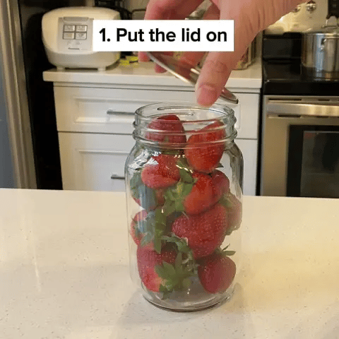 Hand placing a lid on a jar filled with strawberries.