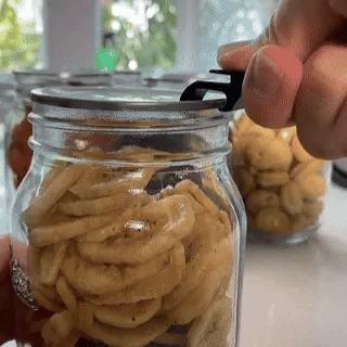 Hand opening a jar of homemade snacks using a tool.