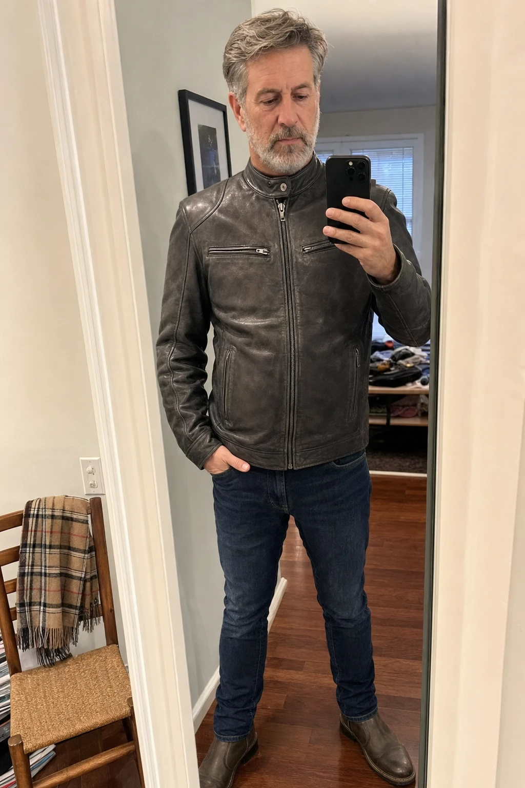 Different mature man taking a mirror photo in a gray leather jacket at home