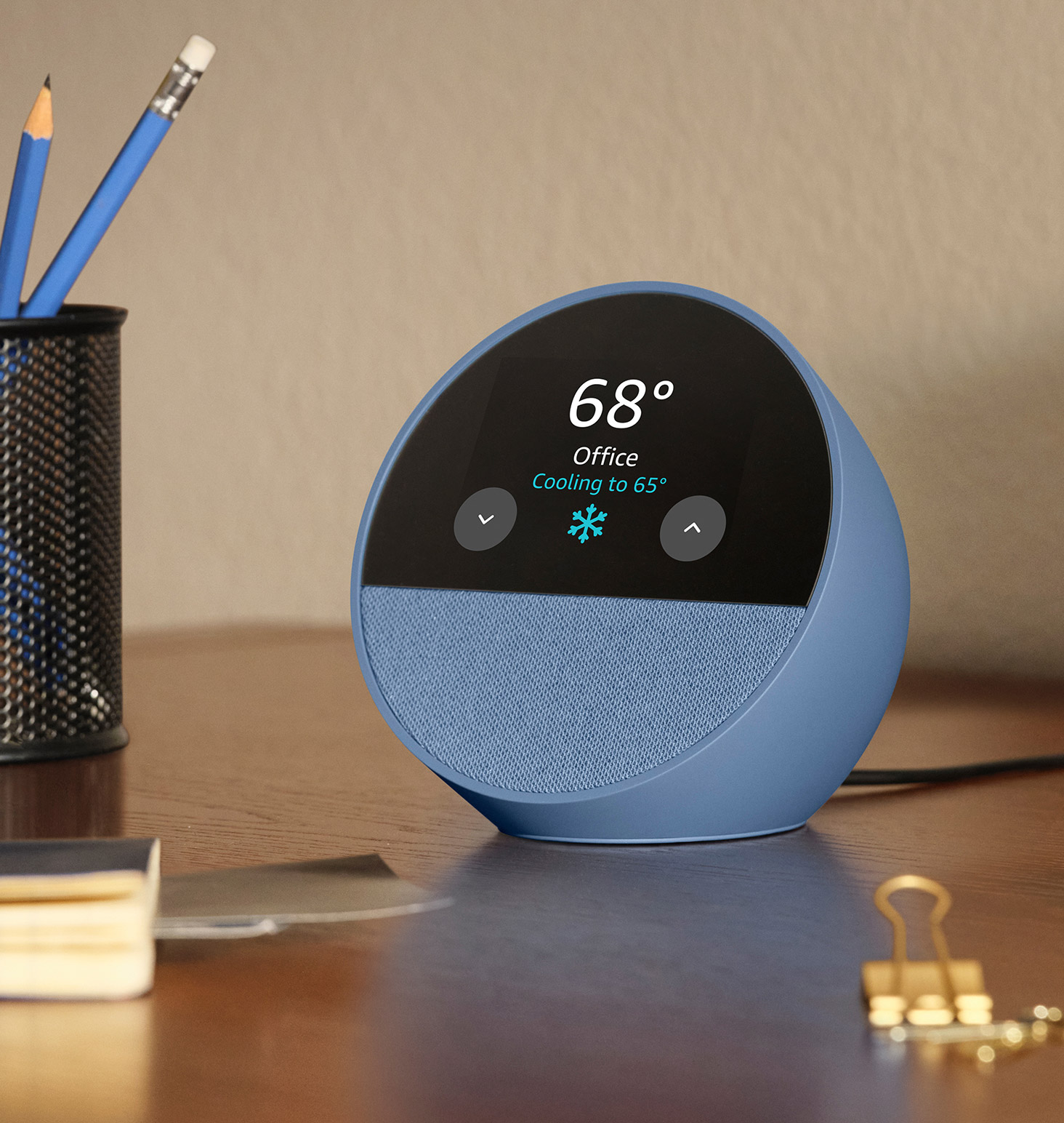 Echo Spot is on a desk. The 2.8-inch display shows the weather and the thermostat in the home office. The thermostat icon shows text "Cooling to 65 degrees." 