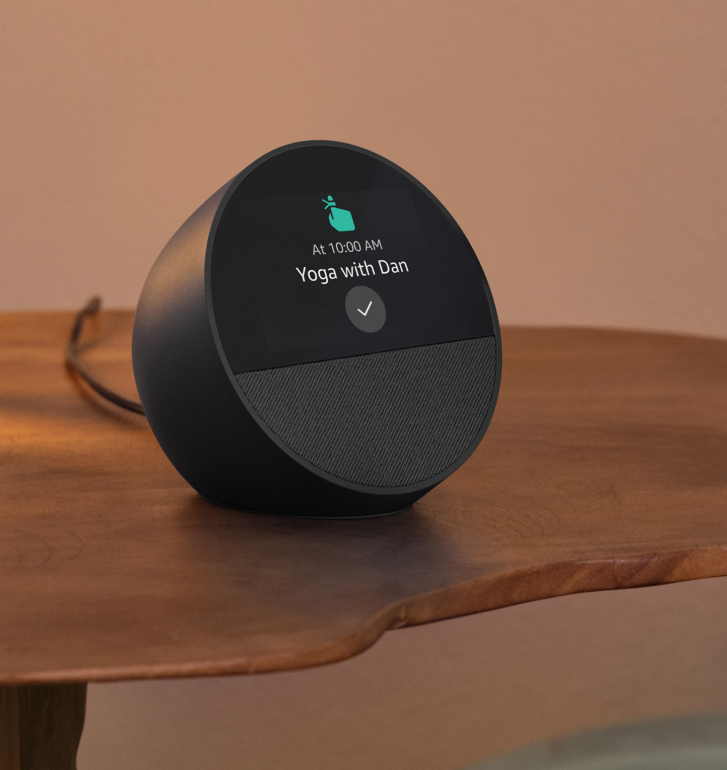 Echo Spot is on a bedside table. The 2.8-inch display shows the reminder "10:00 AM Yoga with Dan" and a pointing finger reminder icon.