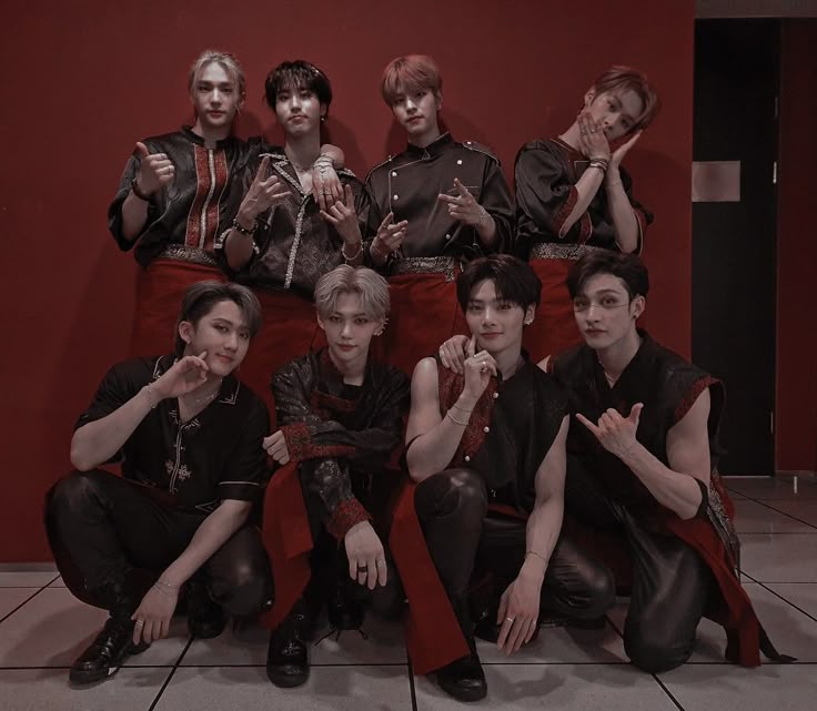 This may contain: a group of young men posing for a photo in front of a red wall with their hands up