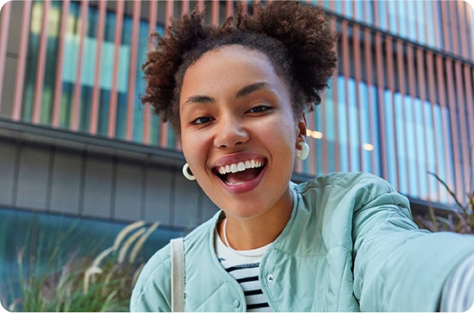A selfie of a smiling woman with a modern building in the background.