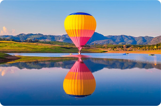 A colorful hot air balloon floating above a lake, with its reflection on the water.