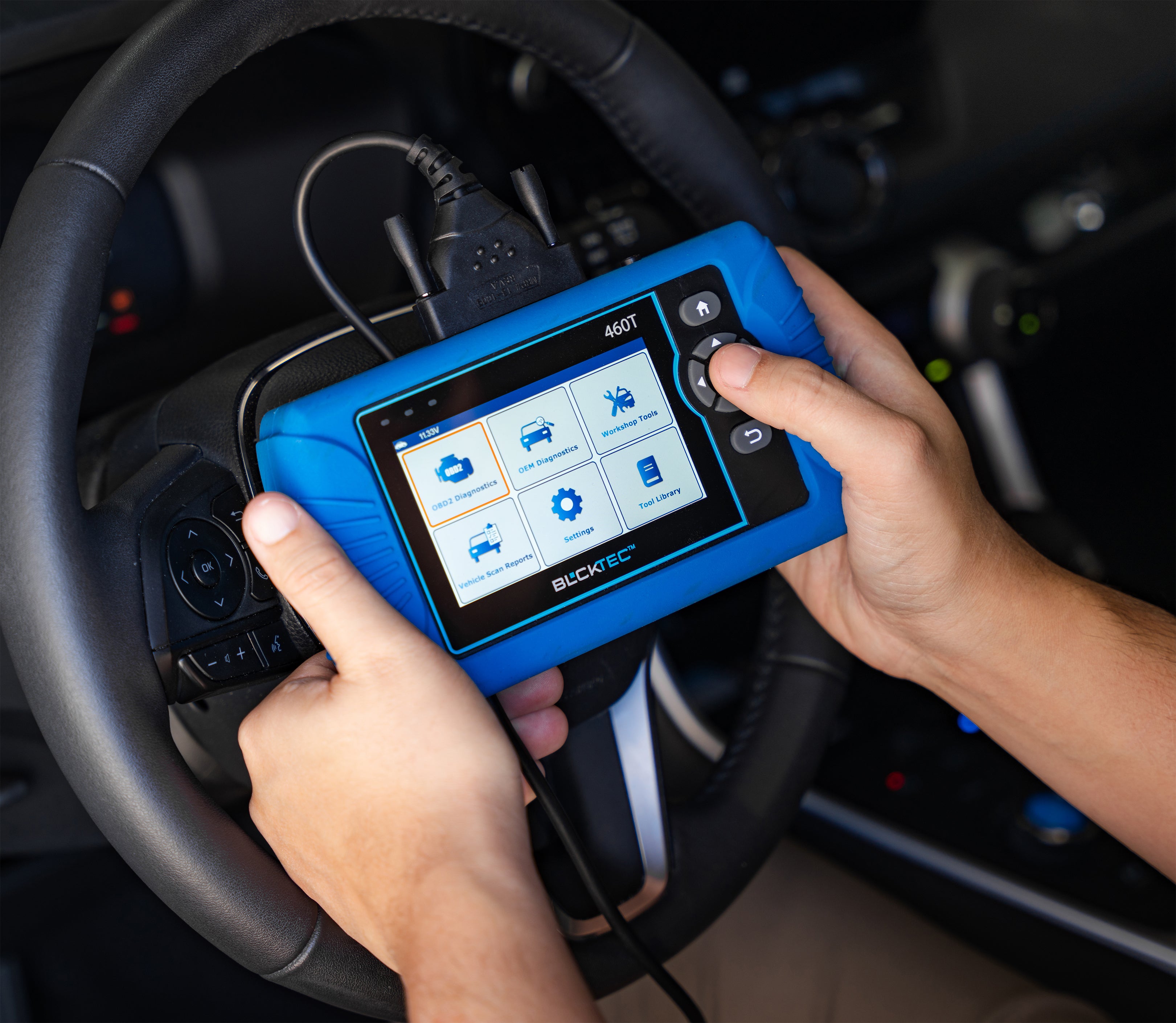 Person holding a diagnostic tool inside a car, displaying various diagnostic options on the screen.