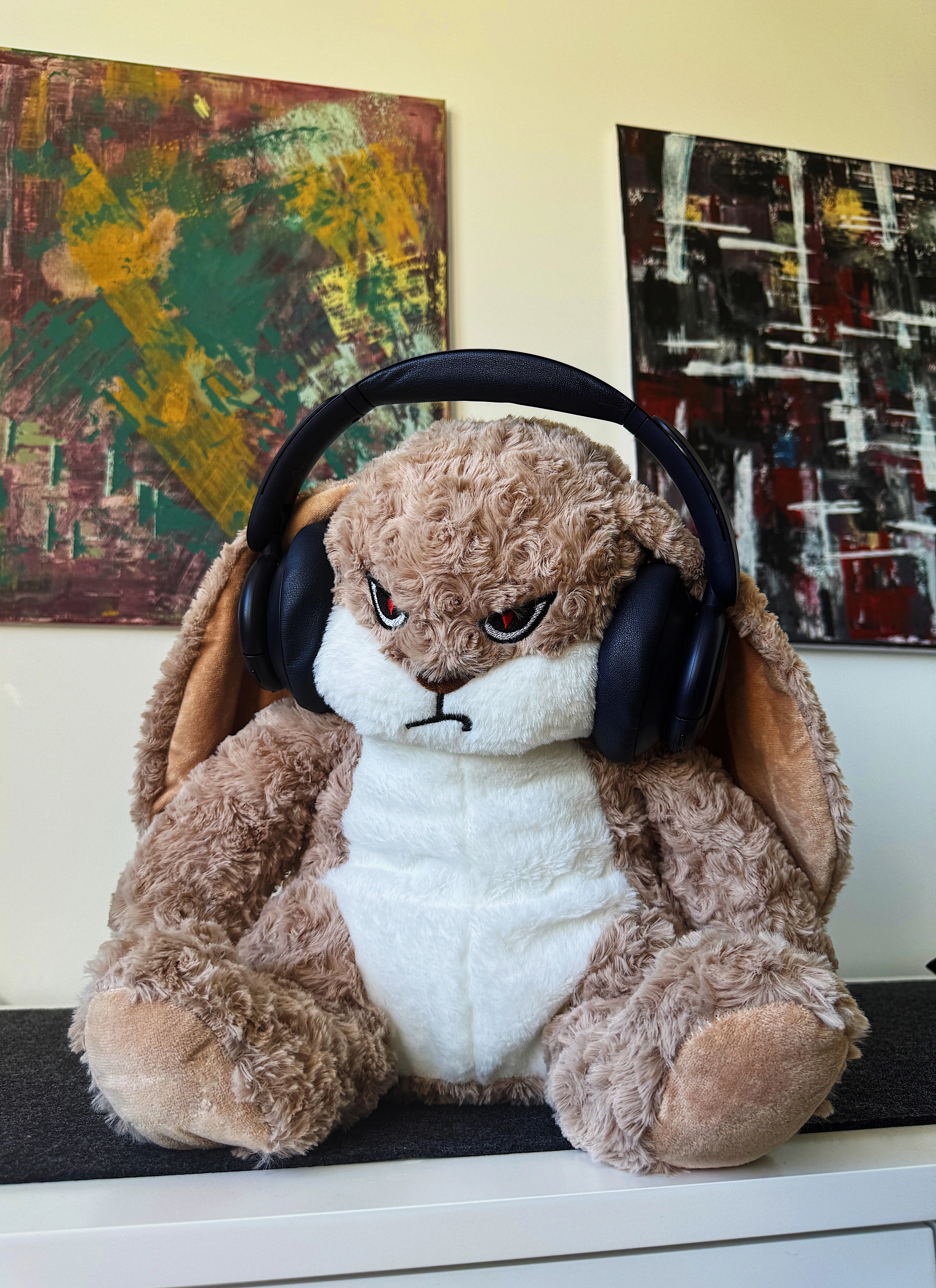 Stuffed moody bunny with headphones on a shelf in front of abstract paintings