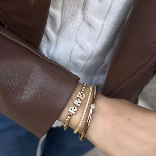 Model wearing a personalized gold bead stretch bracelet with cubic zirconia nameplate on the wrist