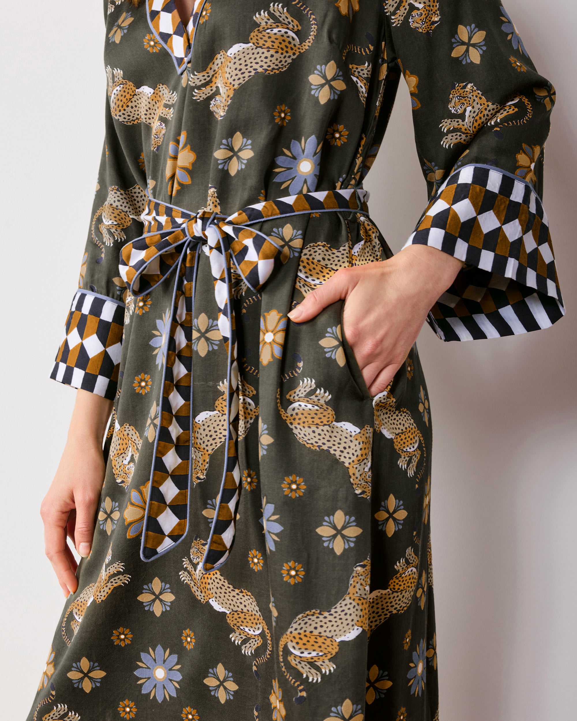 Close view of an olive caftan with spotted leopards, flowers, and geometric trim at the collar, cuffs, and belt.